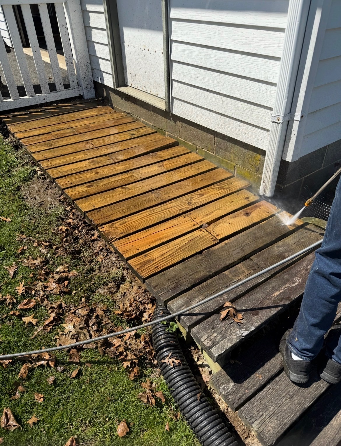 Pressure washing a wood walkway — clean boards on the left, untouched grime on the right.